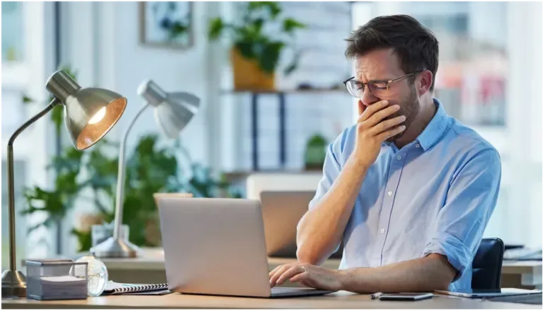 Man yawning at his computer at work